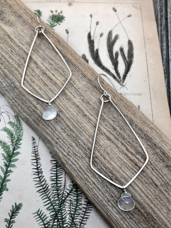 Two elongated diamond shapes, hand-forged from sterling wire are dangled together on a sterling hook.  They are light and airy and swingy and everything you'd want in a statement earring that won't yank your earlobe down to your ankles. Finished with a faceted moonstone teardrop at the bottom and French wires on top.

Product Details:

• Sterling silver
• 2 selenite moonstones
• French ear wires