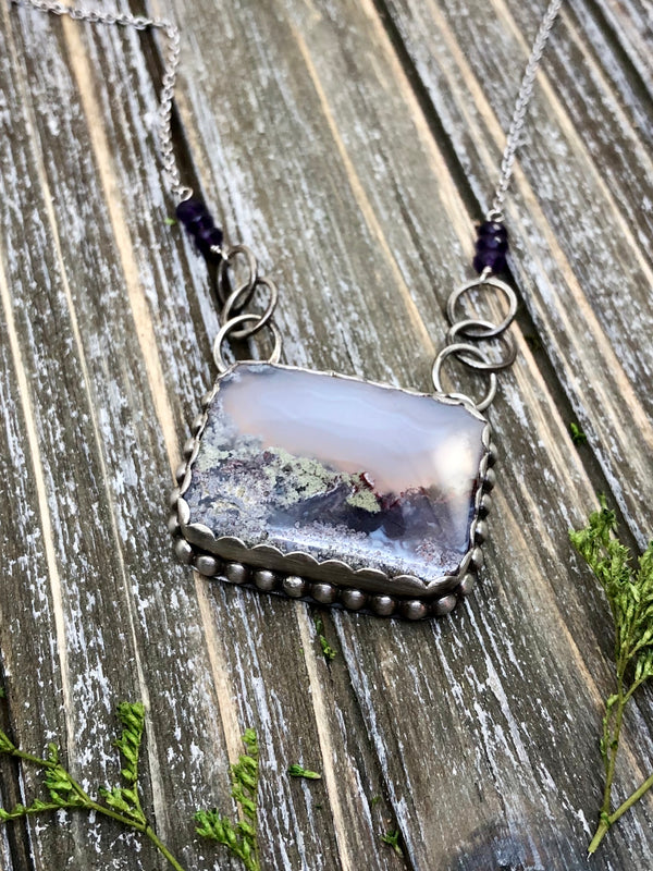 The mountains call to you, as you watch a purple sky put the finishing touches on another gift of a day. I am always appreciative for these moments in time.  Captured here in a lovely lavender rectangle of moss agate and accented with a scalloped bezel, silver beads and handmade chain with amethyst rondelles. 19" with a lobster clasp.

Product Details:

• Indonesian scenic moss agate
• Solid sterling silver
• 6 hand forged chain links
• 6 amethyst gemstones
• Diamond cut cable chain
• 