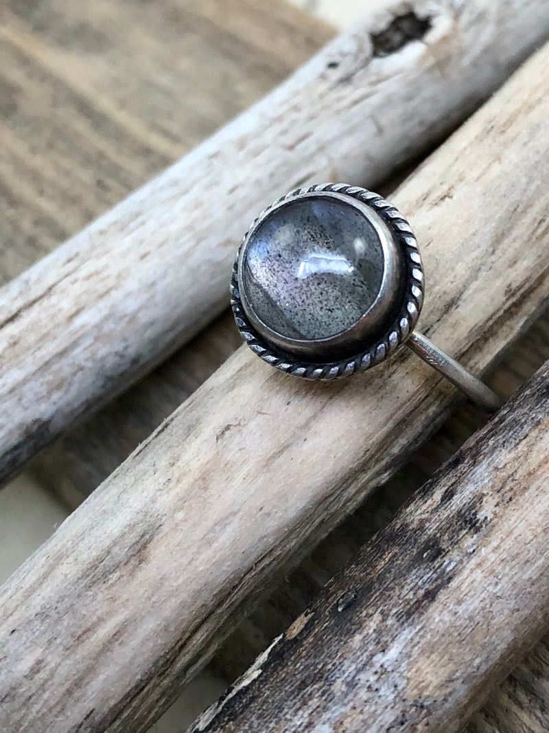 A labradorite with purple flash is bezel set and surrounded by sterling roping.  Finished on a size 7 knife edge shank and antiqued to enhance the fine details.

Product Details:

• Labradorite
• Solid sterling silver
• Size 7