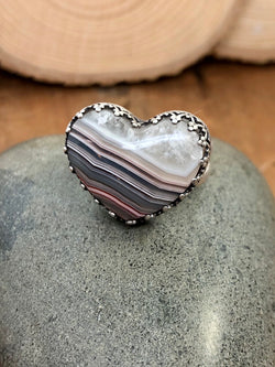 "If we have no peace, it is because we have forgotten that we belong to each other." - Mother Teresa

Find joy, peace, and an everpresent feeling of youthfulness with this heart ring. Set with fancy prongs which are also upside down hearts, this beautiful laguna lace agate heart needs no extra adornment. With a color spectrum from pink to gray to blue to shimmery white crystal, this gem has it all, and so do you. Finished on a split shank size 7 ring, add this beauty to your everyday c