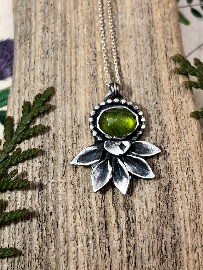 "Be kind, for everyone you meet is fighting a harder battle." - Plato

The most haunting and magical rose cut vesuvianite gem is bezel set and adorned with a silver beaded halo and a lotus flower underneath. Vesuvianite is so named because it was discovered next to Mount Vesuvius. The lotus flower was hand-carved and then cast in sterling silver. This necklace is finished on 16 inches of diamond cut cable chain with a lobster clasp. PLEASE NOTE this piece is a small crack in the back, 