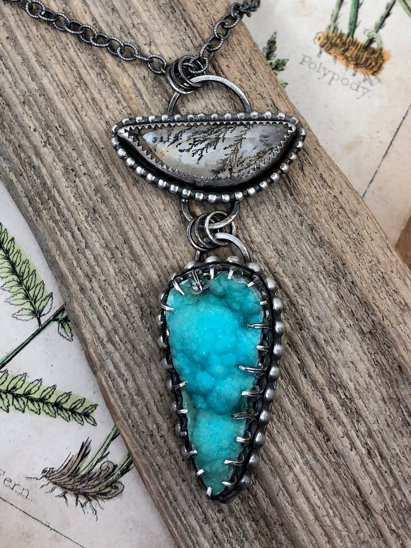 An incredible faceted piece of dendritic quartz in a half moon shape is bezel set and displayed over a sparkling teardrop of chrysocolla in malachite druzy.  Both are set in sterling and embellished by silver balls.  Finished on a 17" oxidized sterling chain with a lobster clasp.

•Half moon shaped dendritic quartz
•Chrysocolla in malachite druzy
•Fine and sterling silver
•17'' oxidized sterling chain with a lobster clasp