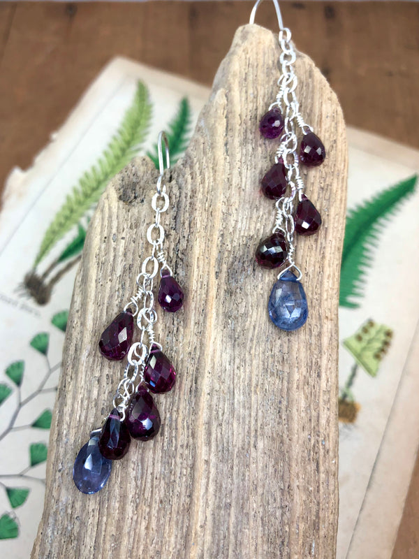 Perfectly crimson rhodolite garnets are displayed on fancy silver chain with a beautiful iolite gem at their focal point. Approximately 2.5” from the hook and finished on sterling French wires.

• 8 - rhodolite garnet briolettes 
• 2 - iolite briolettes 
• Fancy silver chain
• Sterling French wires
