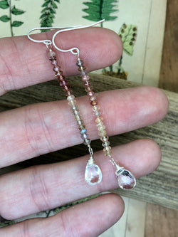 Multi-colored rondelles of tourmaline are wire tied and accented by a sparkling clear quartz briolette in these elegant drop earrings. Approximately 2.5" from the top of the hook. Finished on sterling French wires

• Tourmaline rondelles
• 2 - faceted quartz briolettes
• Sterling French wires