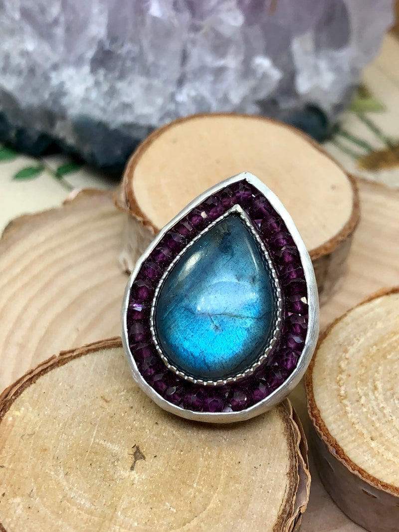 Embrace wonder and enchantment.

Immerse yourself in the perfection of the raindrop form and moody blue hue of this exquisite Labradorite gem. Dramatically set off with rhodolite garnets, this arresting size 7 ring is the perfect for work, informal wear, or special occasions.

•Labradorite gem
•Rhodolite garnet gems
•Fine and sterling silver
•Size 