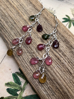 "Be kind, for everyone you meet is fighting a harder battle." - Plato

Bask in the glow of a "watermelon" color palette featuring rich hues of green, magenta, and amber. Pear-shaped and faceted gems are wire wrapped along a silver chain and finished on sterling French wires. A cascade of color perfect for any elegant ensemble.

Product Details:

• Sterling silver ear wires
• Fourteen multi-colored tourmaline briolette gems
• Sterling and fine silver
• Approximately 2" long and just ove
